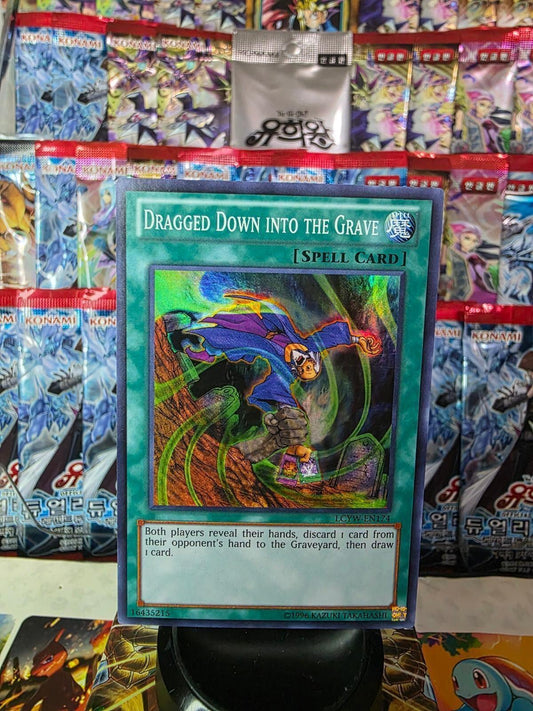 Dragged Down into the Grave Super Rare Yu-Gi-Oh! spell card with holographic foil in front of booster packs.