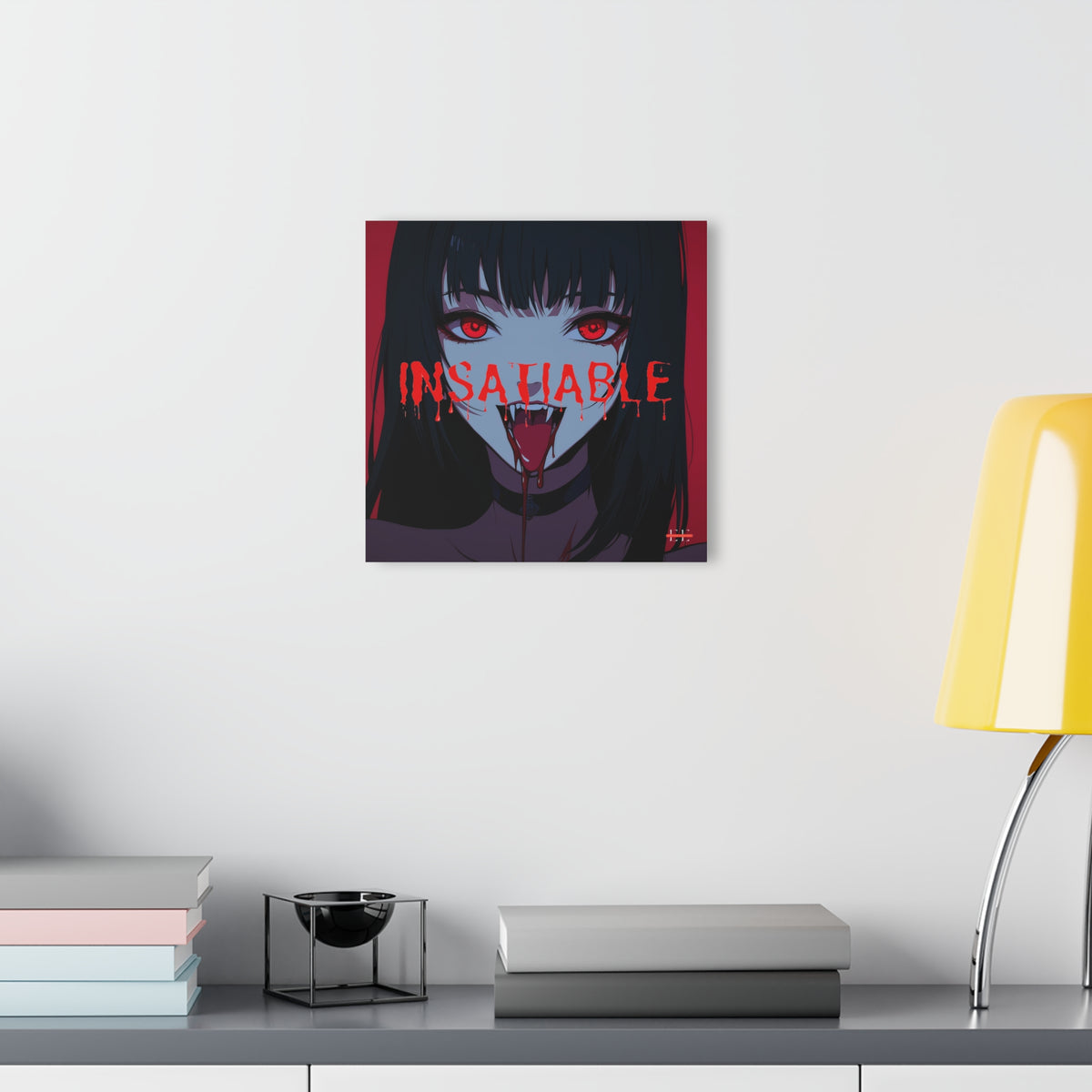 "INSATIABLE" acrylic masterpiece hanging on a white wall above books and a yellow lamp.