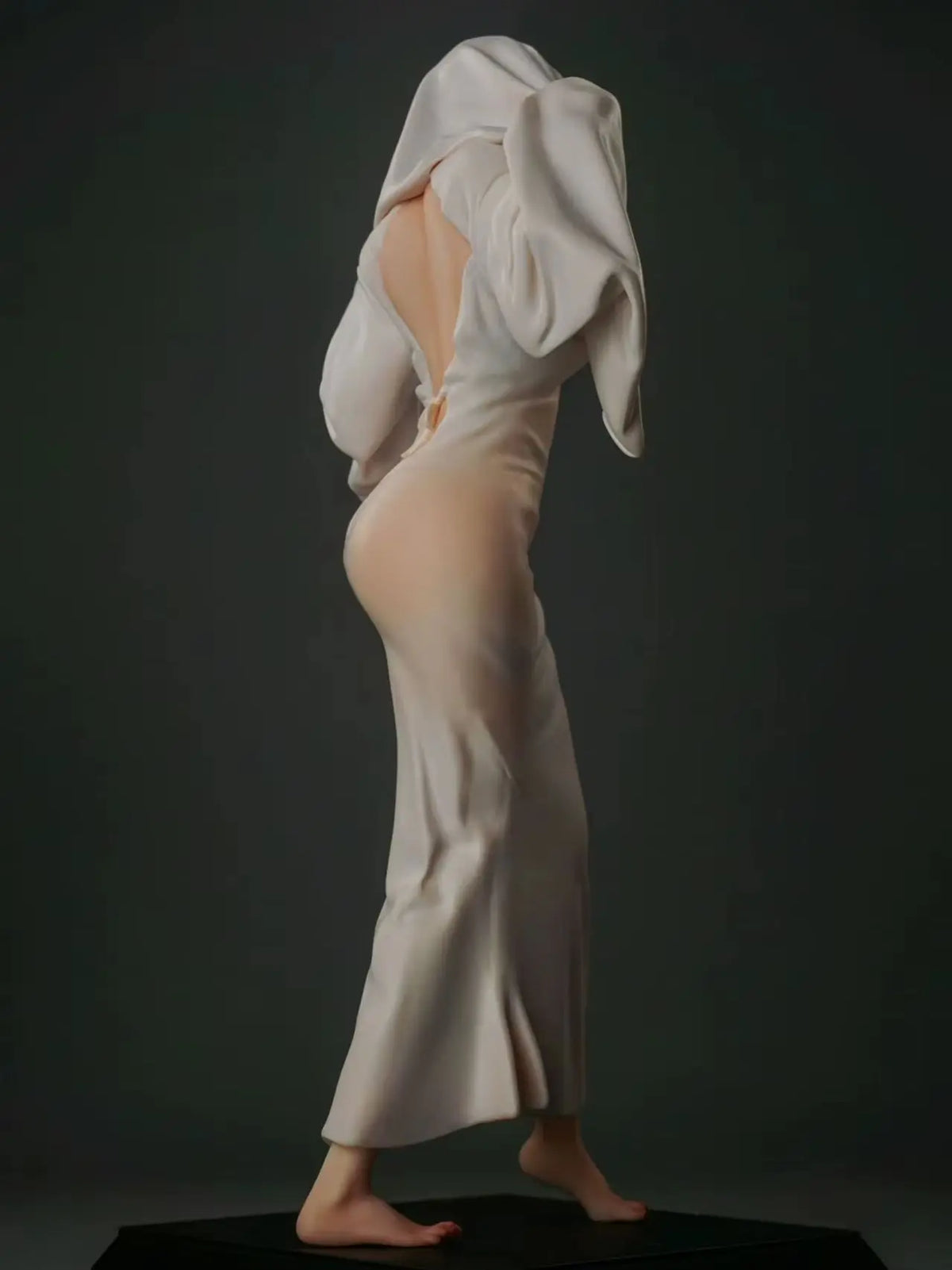 Figurine of a woman wearing a long white dress and hood, viewed from the back against a dark background.
