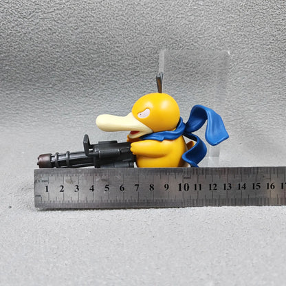 A yellow duck figurine with a blue scarf holds a black Gatling gun, with a metal ruler placed below it.
