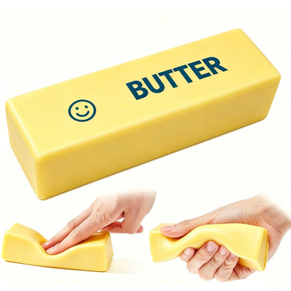 A yellow butter-stick stress toy printed with a smiley face and "BUTTER" is squeezed and depressed by hands.