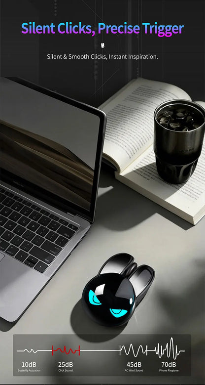 Black rabbit-shaped wireless mouse with glowing blue eyes, on a desk with a laptop, book, and tumbler.