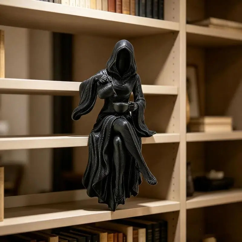 A black, hooded grim reaper figurine sits on a bookshelf shelf, holding a small cup.