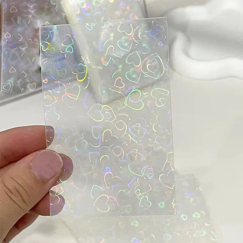 Clear card sleeve with a holographic laser foil heart pattern, held by fingers.