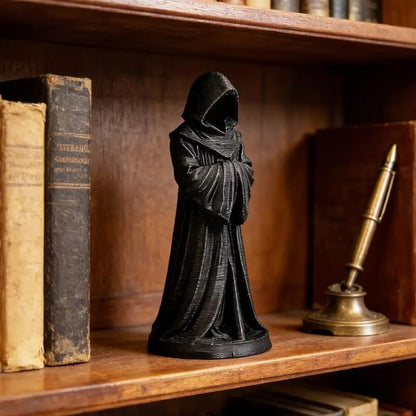 Black robed statue with a hooded figure standing between old books and a pen on a shelf.
