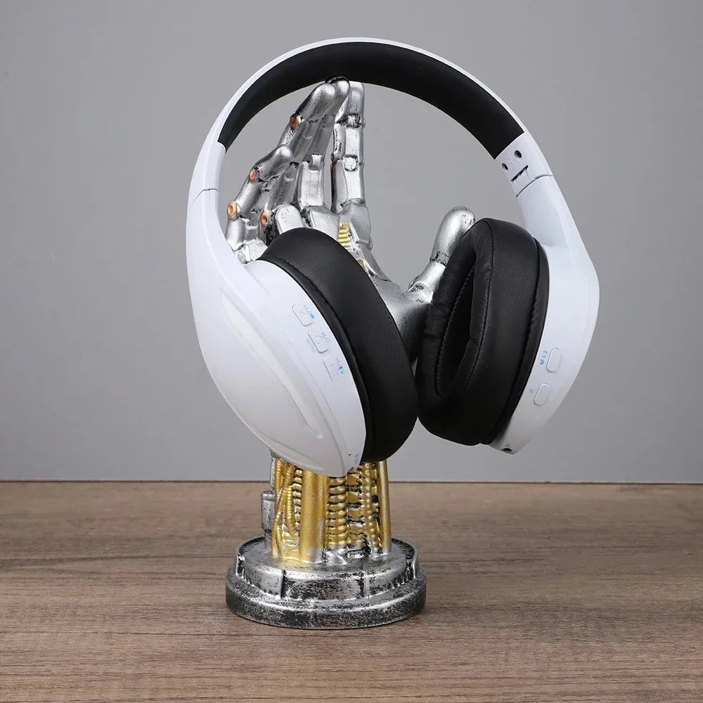 A silver and gold robotic hand stand holds white and black over-ear headphones on a wooden surface.