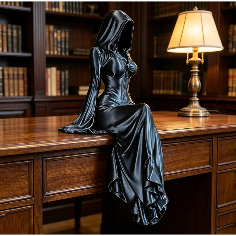 A black, hooded female reaper figurine sits on a wooden desk, her draped dress cascading down.
