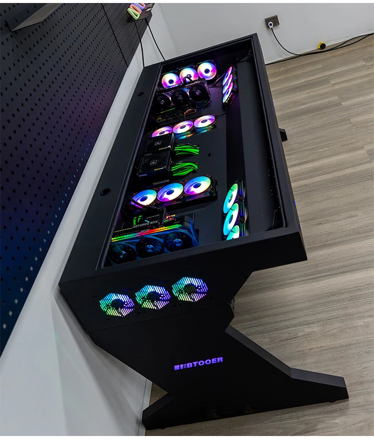 Black dual-system computer desk with integrated chassis, glowing RGB fans, and visible internal components under glass.