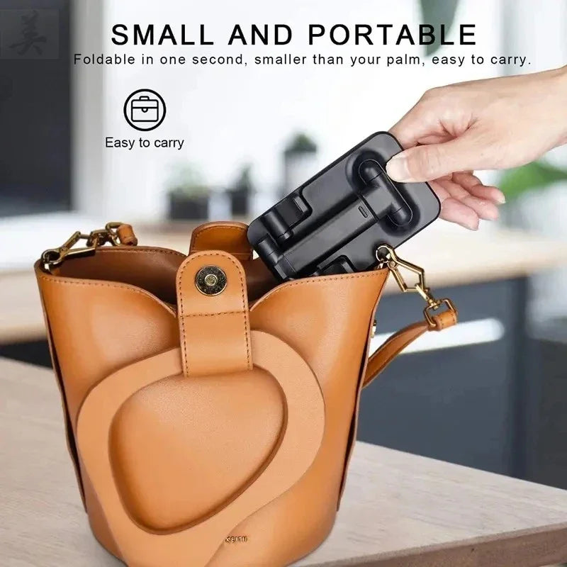A hand places a folded black phone stand into a tan leather handbag.