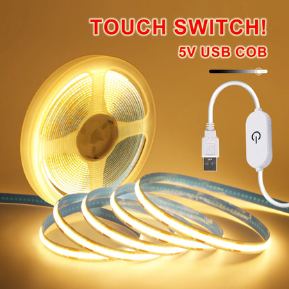 A glowing warm white COB LED strip light on a spool and in loose loops, featuring a USB cable and touch switch.
