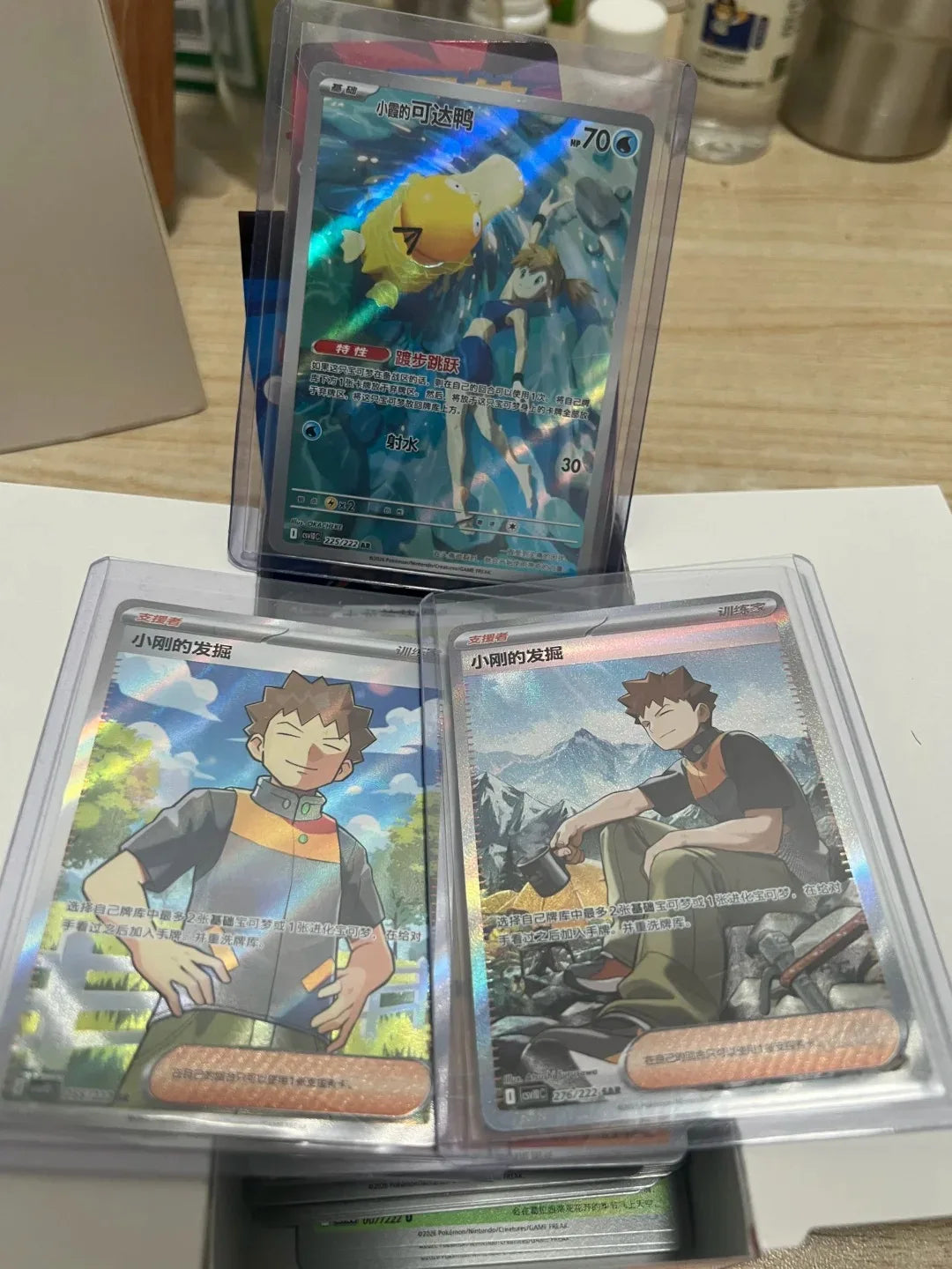 Three Pokémon trading cards in protective sleeves, featuring Psyduck and Misty, and two featuring Brock.