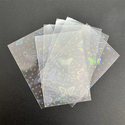 Clear holographic card sleeves featuring a laser butterfly and floral pattern, stacked on a dark surface.