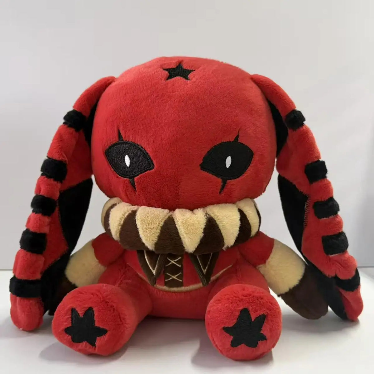 Red and black rabbit plush with long striped ears, black eyes with tear drops, a ruff, and black star accents.