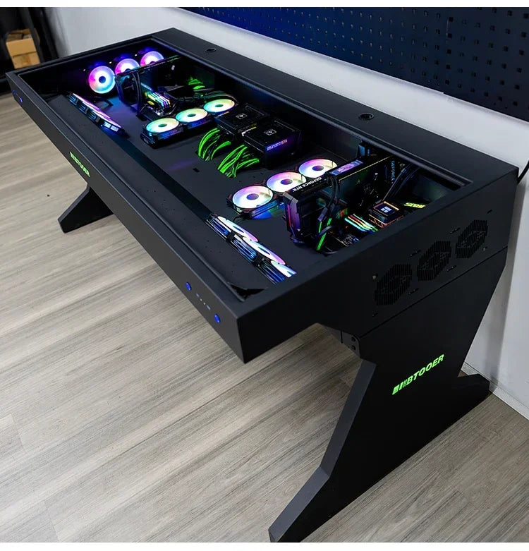 Black computer desk with an integrated glass-top chassis holding two custom PC builds featuring RGB fans.