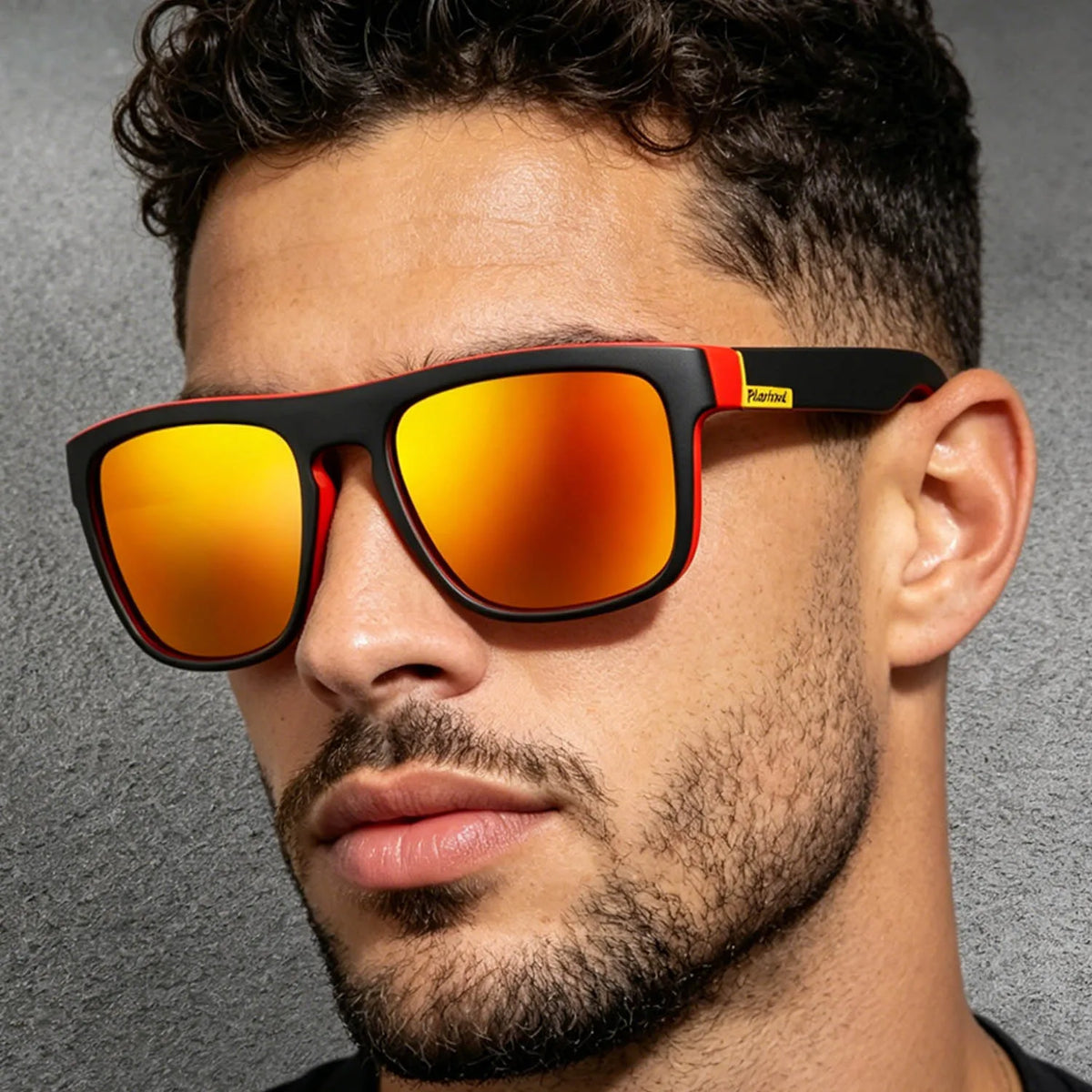 A man with dark curly hair wears square sunglasses featuring matte black and red frames with bright orange mirrored lenses.