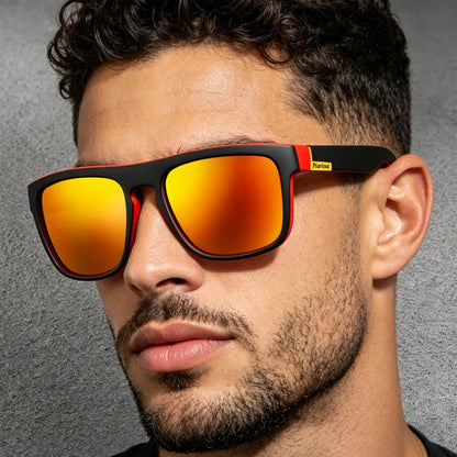 A man with dark curly hair wears square sunglasses featuring matte black and red frames with bright orange mirrored lenses.