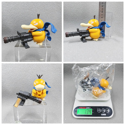 Yellow Psyduck figurine wearing a blue scarf and holding a large grey Gatling gun.