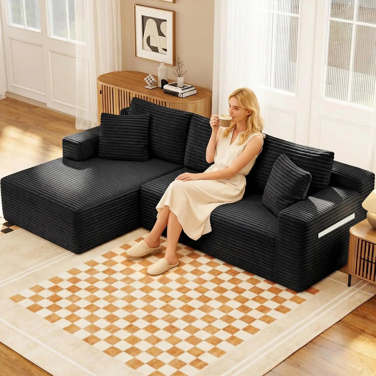 Black corduroy L-shaped sectional sofa with chaise, back cushions, and two throw pillows in a modern living room.