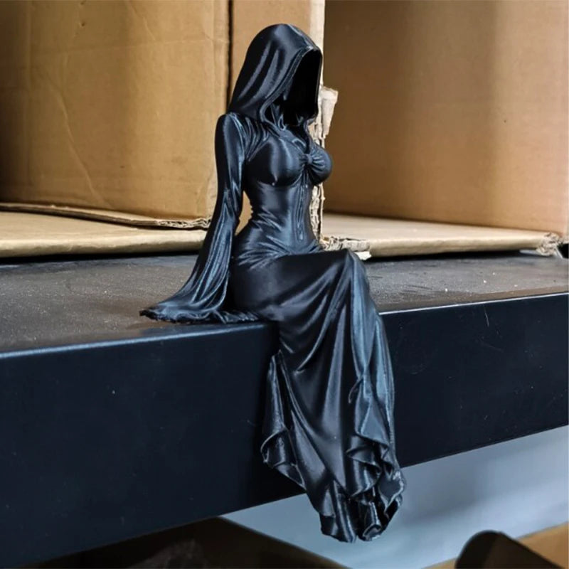 A black figurine of a hooded female figure sitting with her legs dangling down.