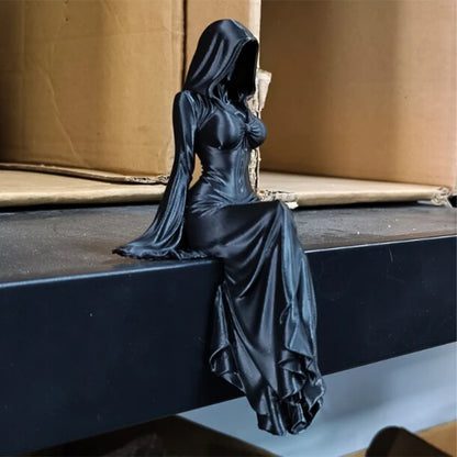 A black figurine of a hooded female figure sitting with her legs dangling down.