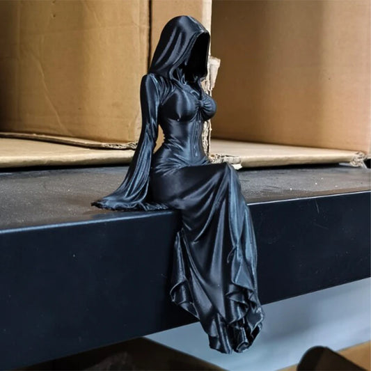 A black figurine of a hooded female figure sitting with her legs dangling down.