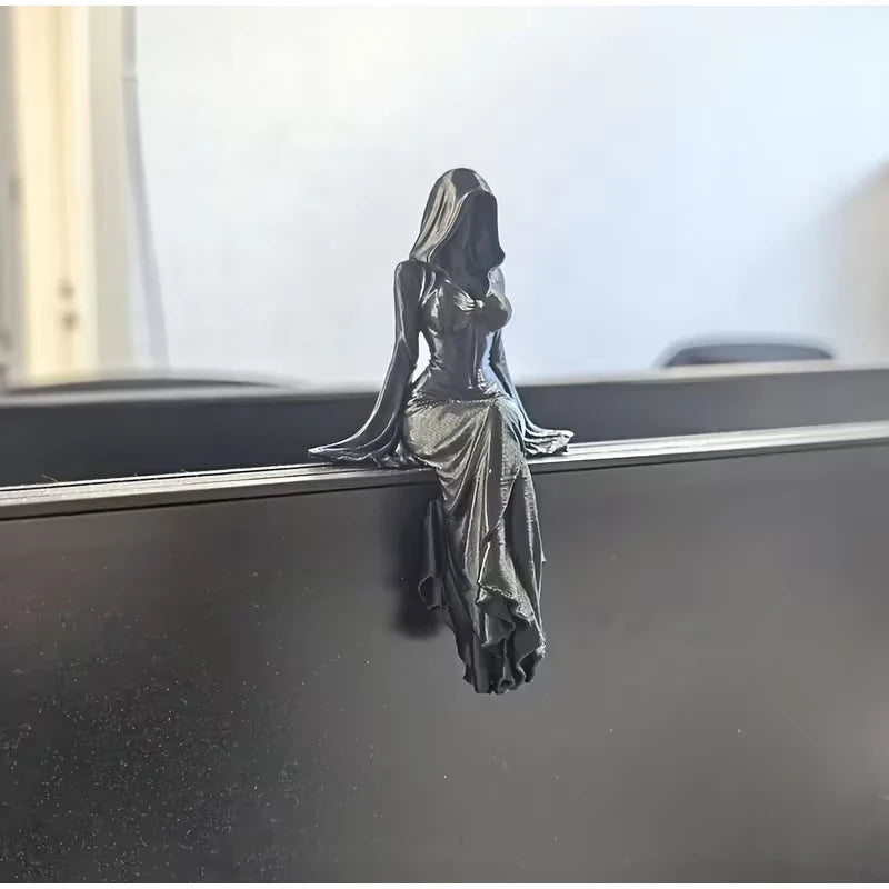 A black hooded female figurine sits on a ledge, her draped dress hanging down.