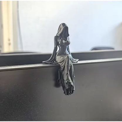 A black hooded female figurine sits on a ledge, her draped dress hanging down.