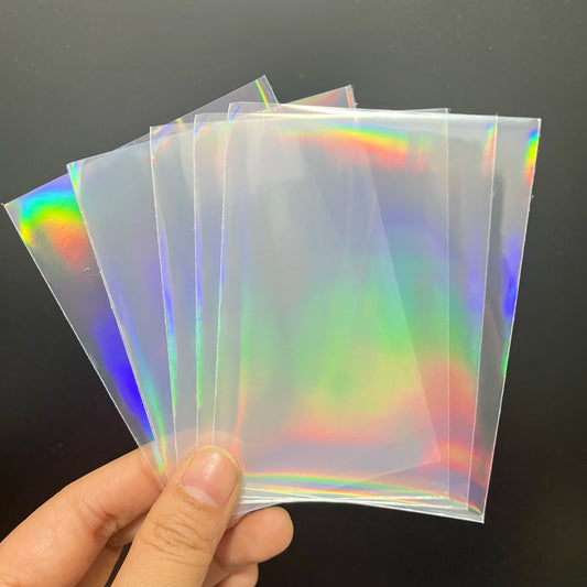 Fanned-out translucent card sleeves with a vibrant rainbow holographic foil effect held by a hand.