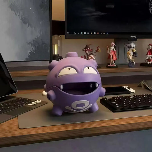 A purple Koffing storage box and incense holder on a desk with a computer keyboard and anime figures.