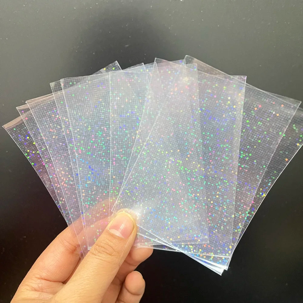 A hand fans out transparent holographic card sleeves with a tiny laser-foil dot pattern.