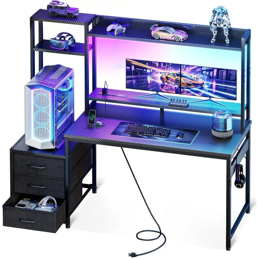 Black gaming desk with carbon-fiber-texture surfaces, hutch, RGB lights, monitor shelf, and three lower fabric drawers.