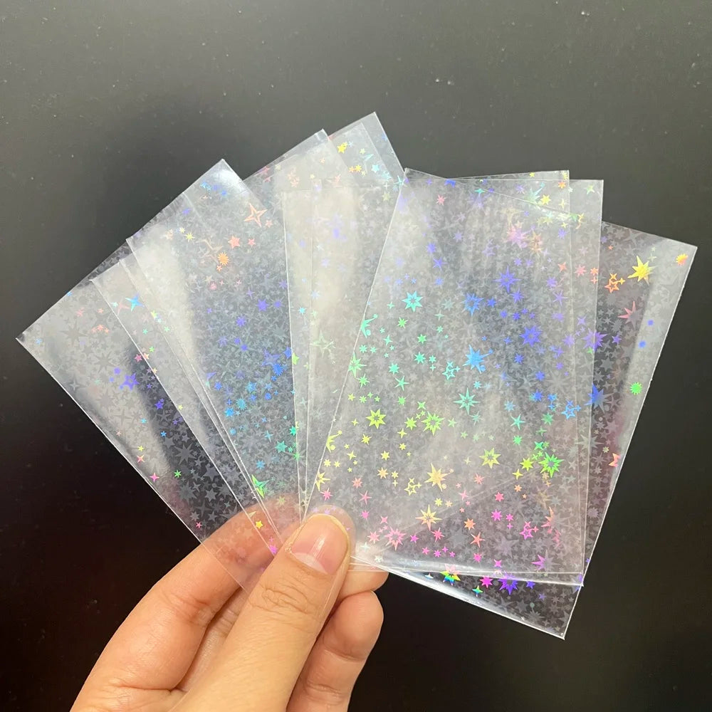A hand holds a fan of clear trading card sleeves with a holographic star foil pattern.