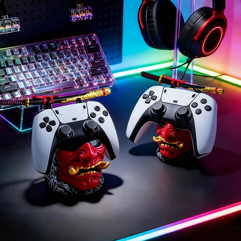 Two red and gold oni mask stands hold white game controllers and miniature samurai swords on a desk.