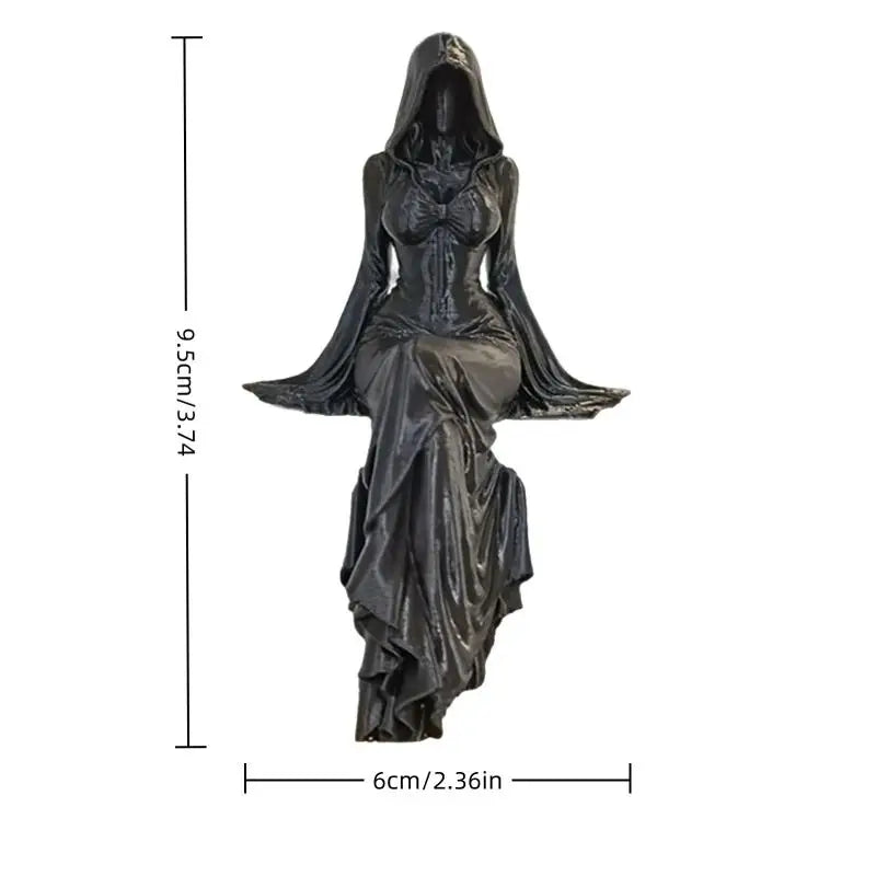 A black resin statue of a hooded female figure sitting, with draped robes, measuring 9.5cm tall and 6cm wide.