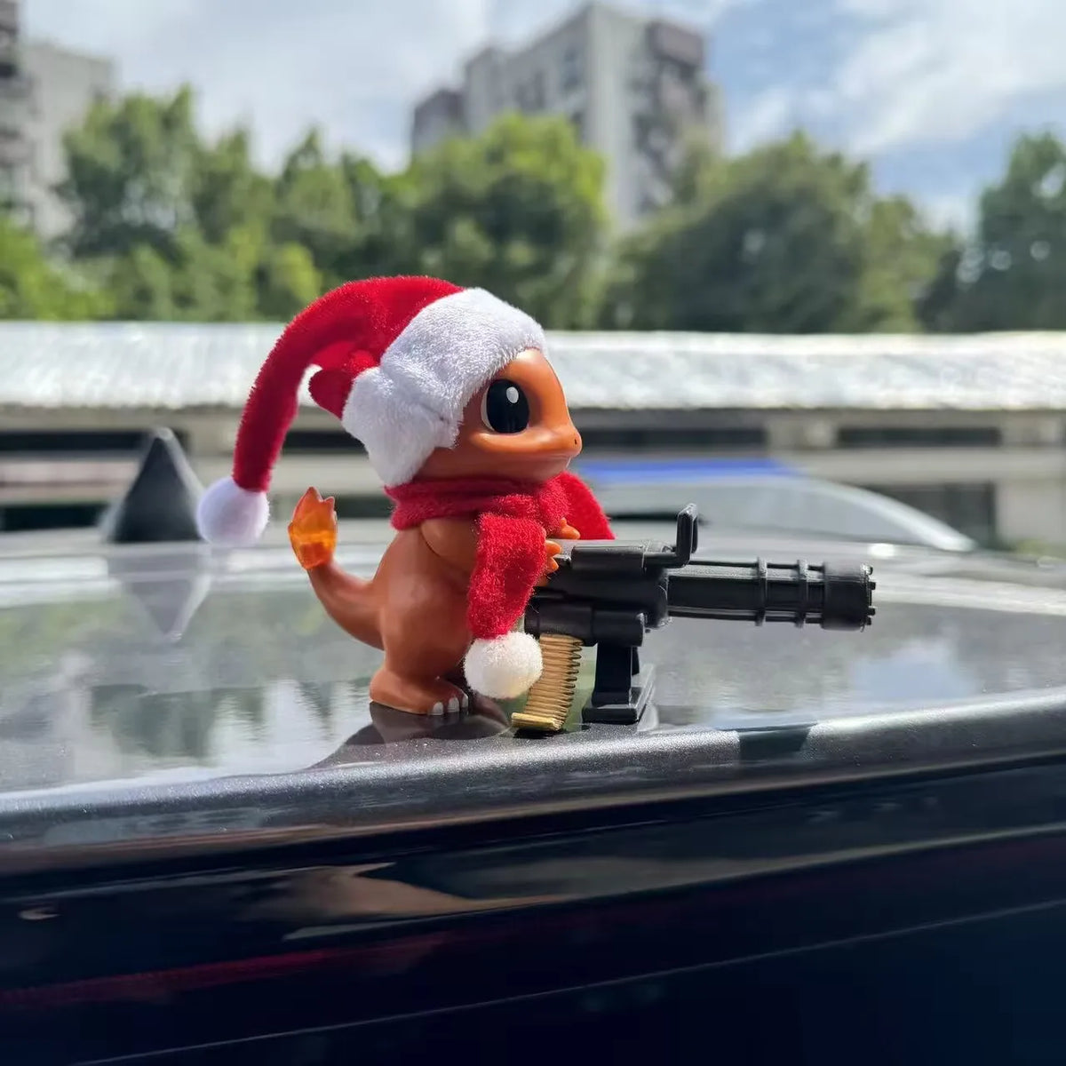 Charmander figurine wearing a red Santa hat and scarf, holding a black Gatling gun.