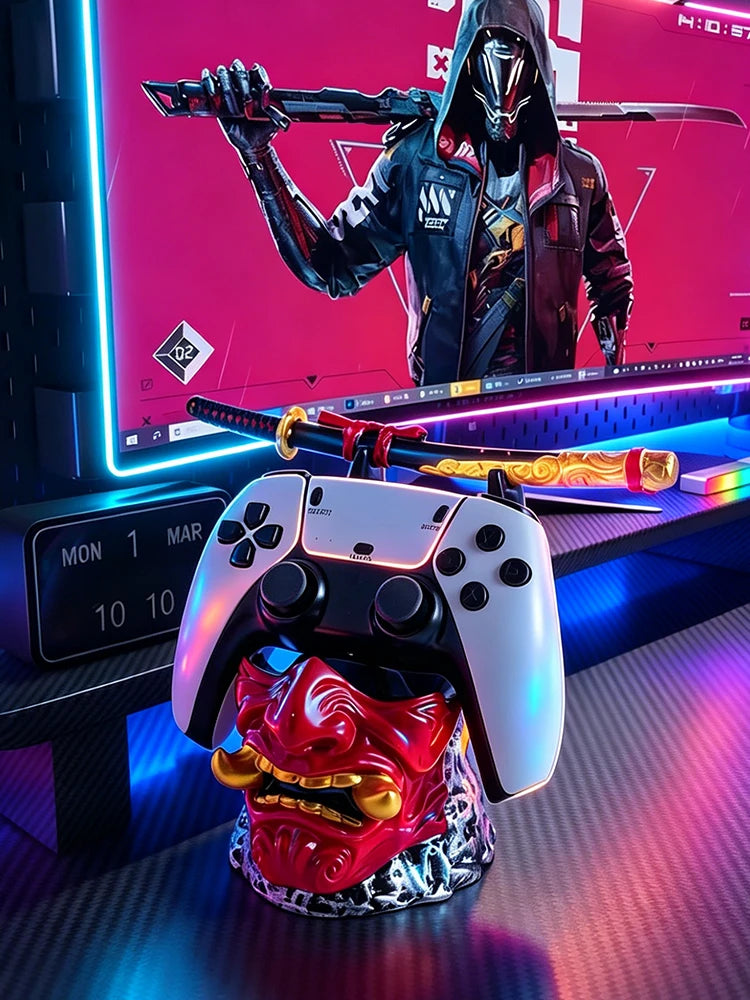 Red and gold oni mask holder supporting a white game controller and a katana on a desk.