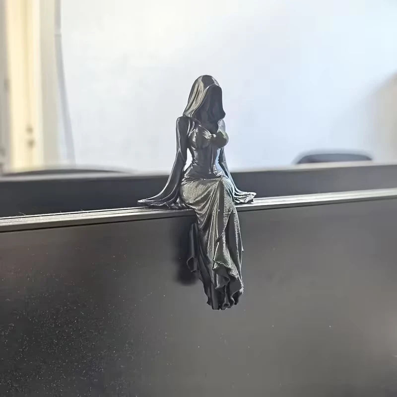A dark, glossy figurine of a hooded female figure sitting with legs dangling over a ledge.