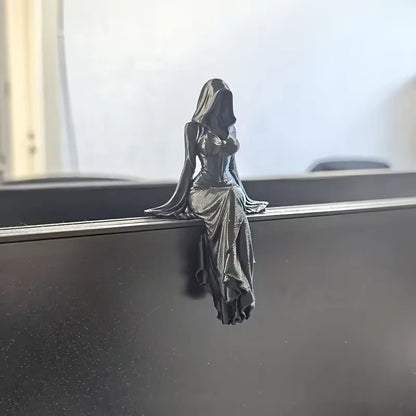 A dark, glossy figurine of a hooded female figure sitting with legs dangling over a ledge.