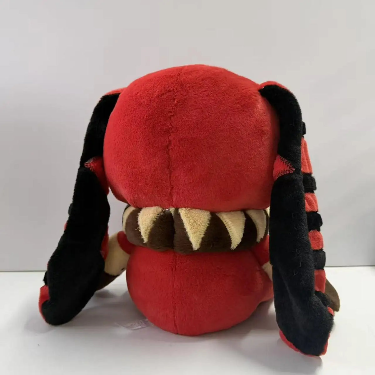 Back of a red plush toy with long black floppy ears, a ruffled collar, and striped details.