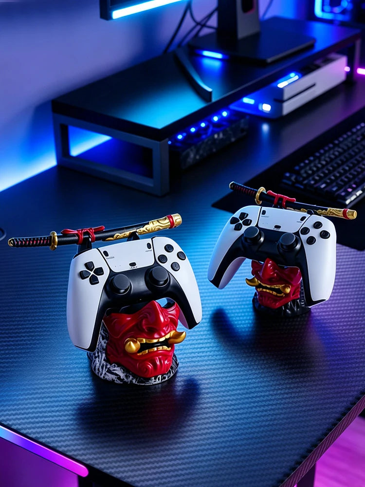 Two red and gold oni mask stands on a desk holding white and black game controllers, each topped with a small samurai sword.