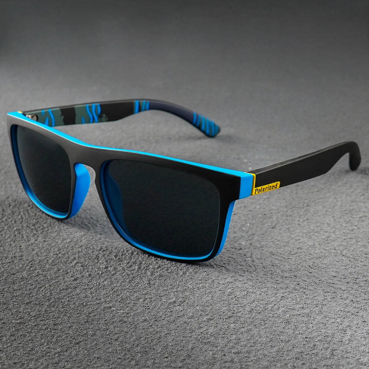 Square polarized sunglasses with matte black frames, bright blue accents, and dark lenses on a gray surface.