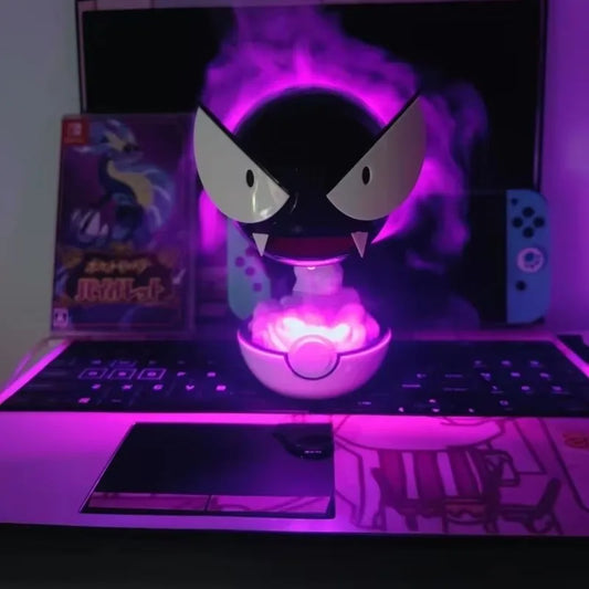 A black Gastly figure sits above a glowing pink Poké Ball, surrounded by purple mist, on a laptop keyboard.