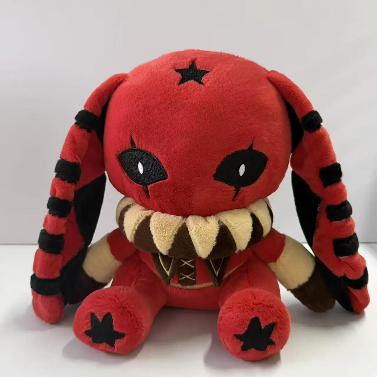 Red plush rabbit toy with long, black-striped ears, large black eyes, a black star on its head, and a ruffled beige collar.