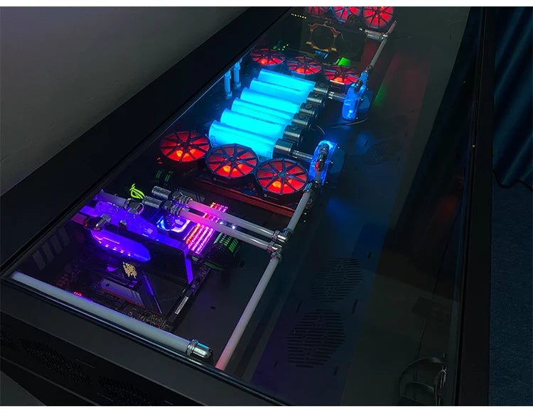 A large black desk with an integrated computer chassis, featuring glowing blue water-cooling tubes and red fans.