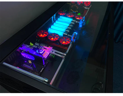 A large black desk with an integrated computer chassis, featuring glowing blue water-cooling tubes and red fans.