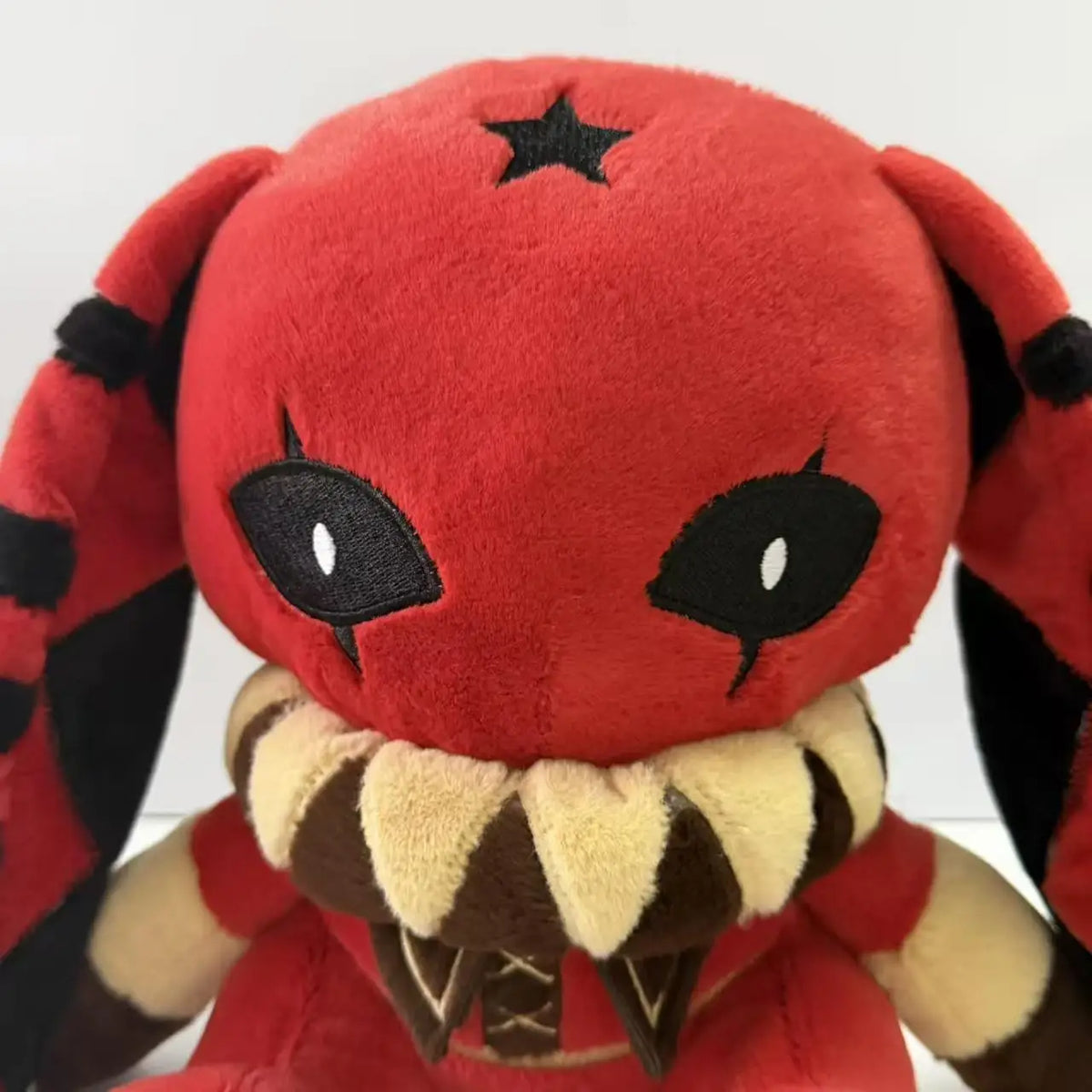 Red plush toy with black star on head, long striped ears, black eyes with white pupils, and ruffled collar.