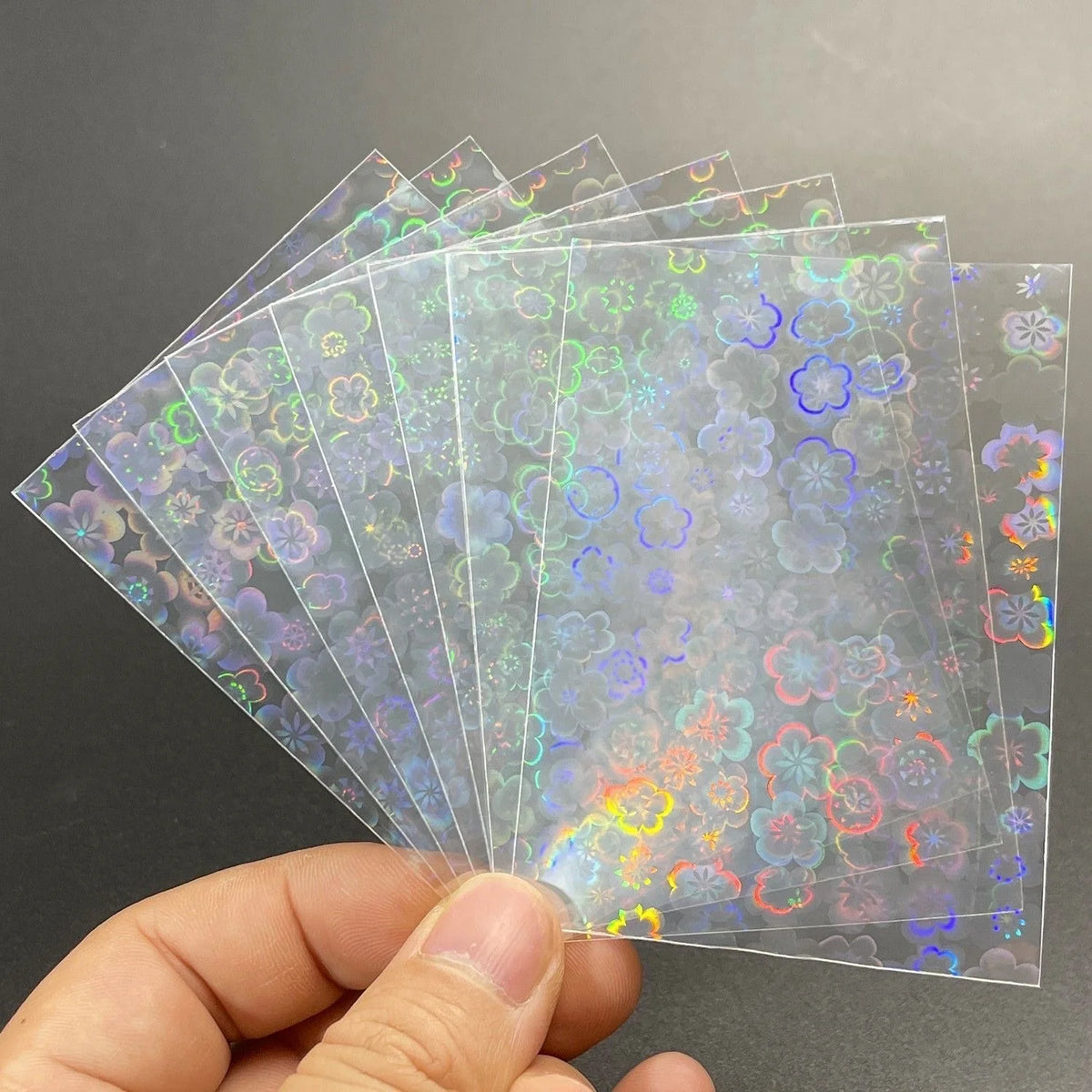 Fanned clear card sleeves feature a holographic laser foil pattern of various sized cherry blossoms.