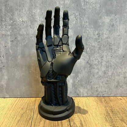 Matte black robotic hand sculpture with segmented fingers, exposed cables, and a round base on a wood surface.
