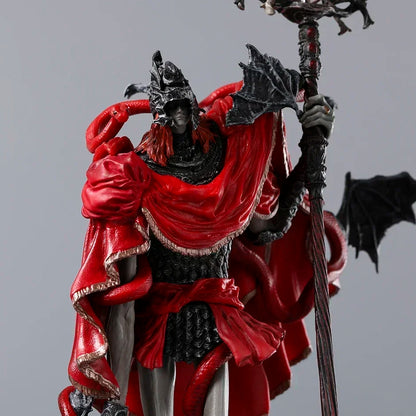 A figurine wearing a black-and-silver helmet and scale armor, a red cloak with gold trim, and holding a tall staff.