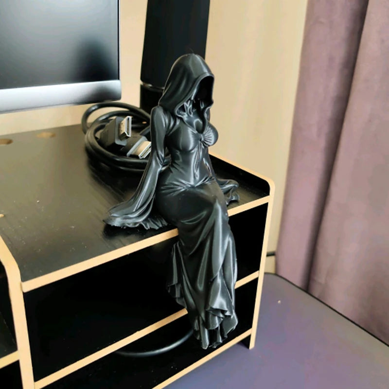Black hooded female statue sitting on the edge of a desk, wearing a long flowing dress.